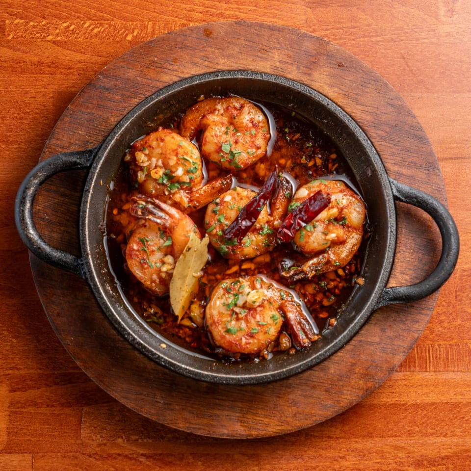 Sizzling Spanish garlic shrimp (gambas al ajillo) in a black skillet on a wooden board.