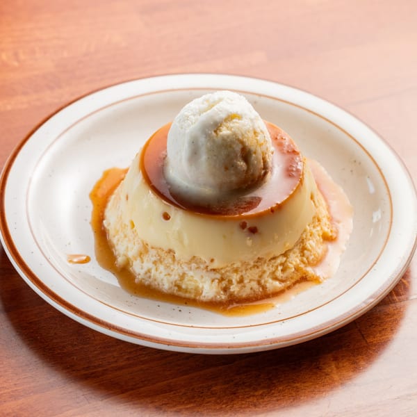 A Spanish flan dessert with caramel sauce and a scoop of vanilla ice cream on a white plate.