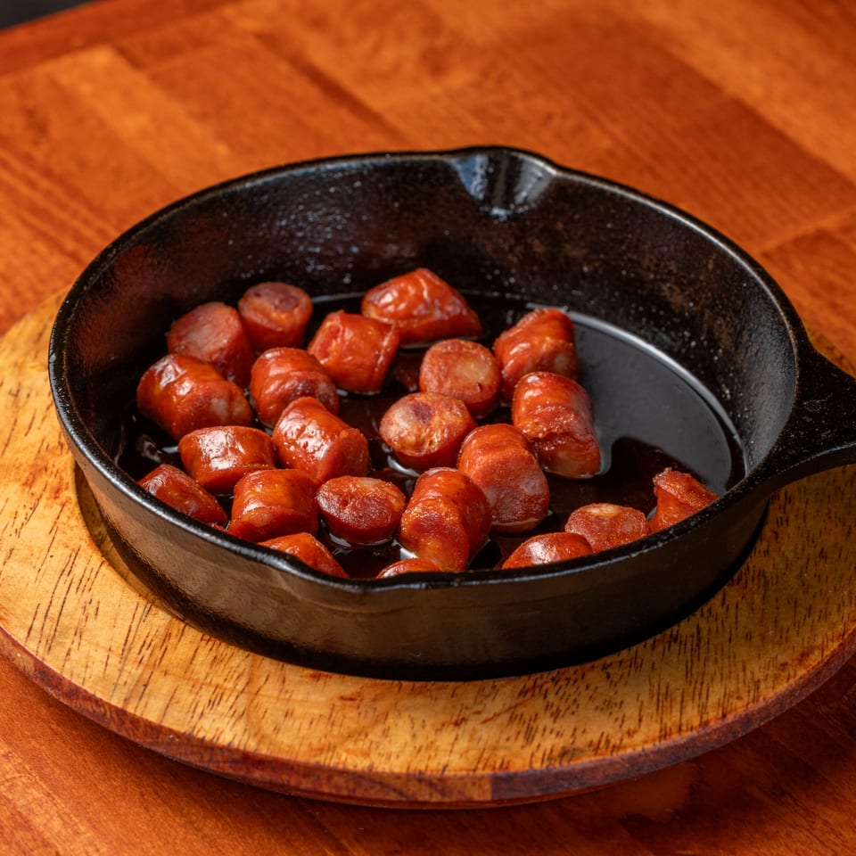 Sizzling Spanish chorizo sausage slices in a black cast iron pan on a wooden table.