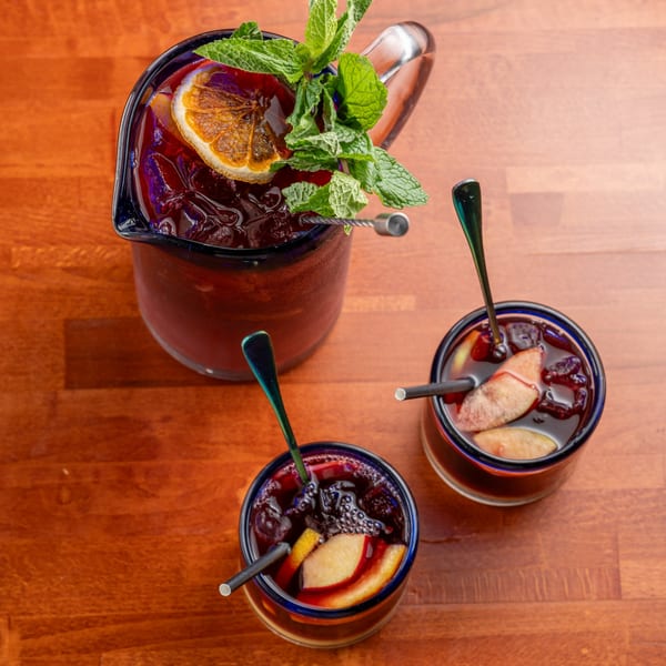 A pitcher of red sangria with orange and mint, and two glasses of sangria with fruit slices.