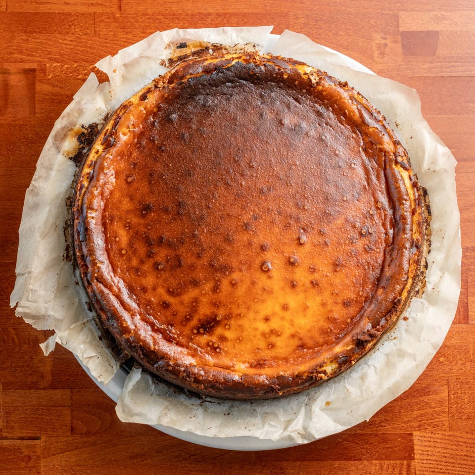 A whole, round Basque cheesecake with a deeply caramelized, dark brown top, on parchment paper.